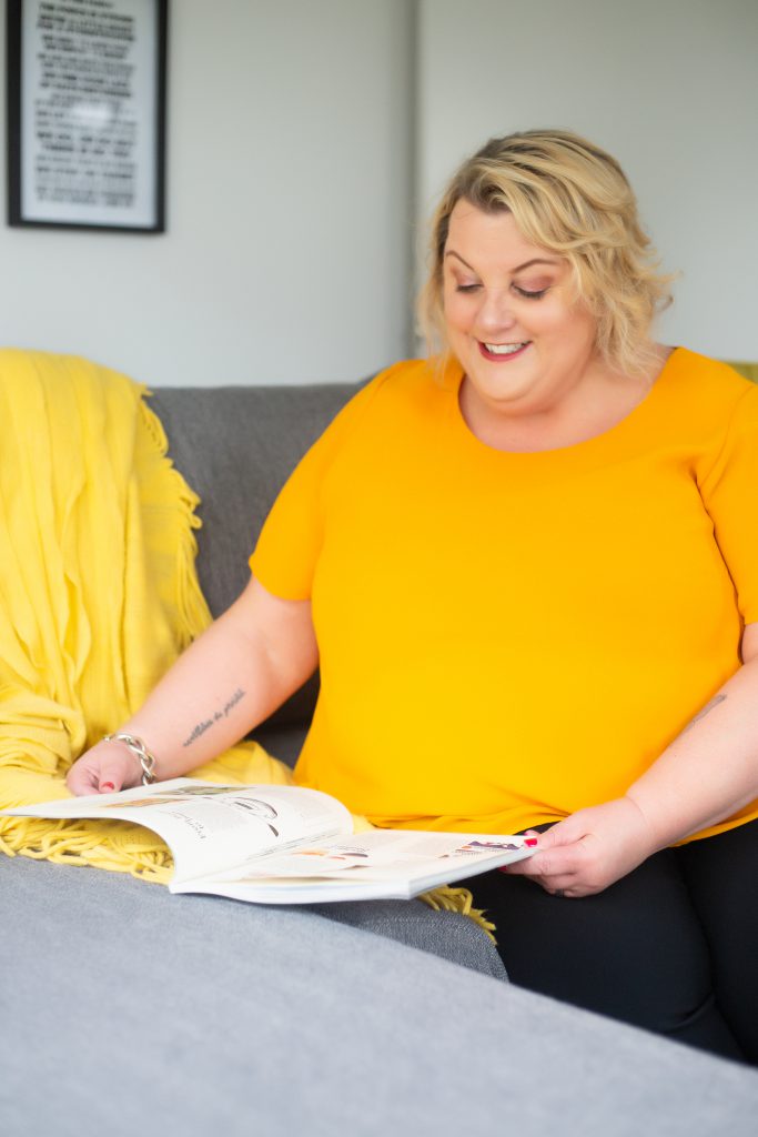 woman in mustard top reading a magzine on a couch