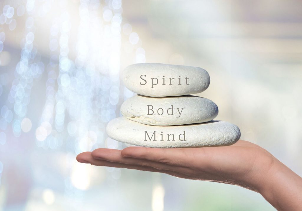 hand balancing three stones with mind body spirit on them