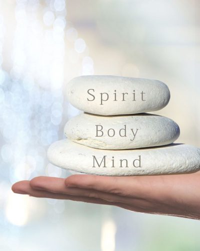 hand balancing three stones with mind body spirit on them