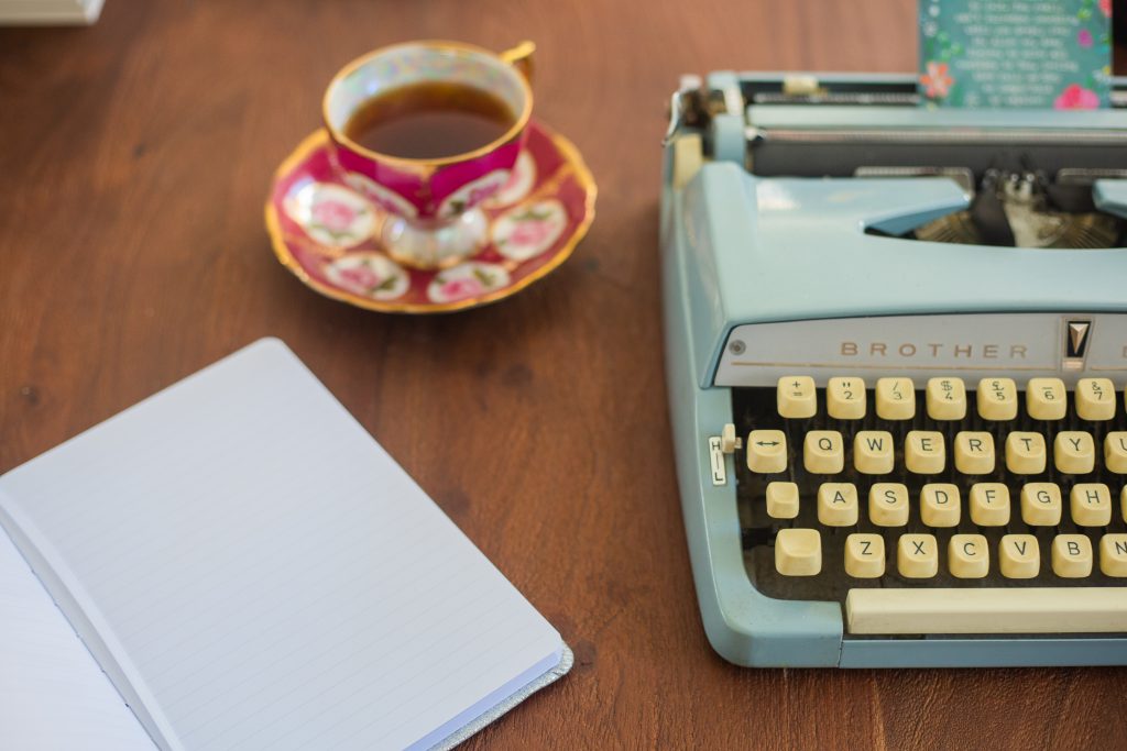 table with teacup typewriter and lined notebook with blank page