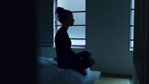 women sitting on end of bed cross legged meditating