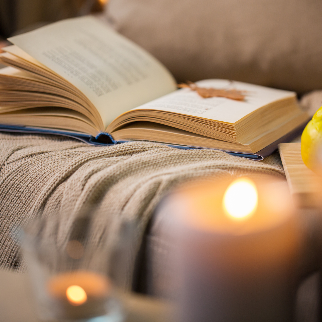 autumn-inspired cosy nook: A book, blanket, and candle, encouraging you to slow down and reconnect with yourself during autumn.