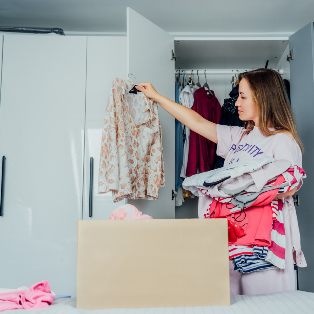 woman decluttering her wardrobe in a bedroom, She is holding clothes and determining what should stay and go. 
